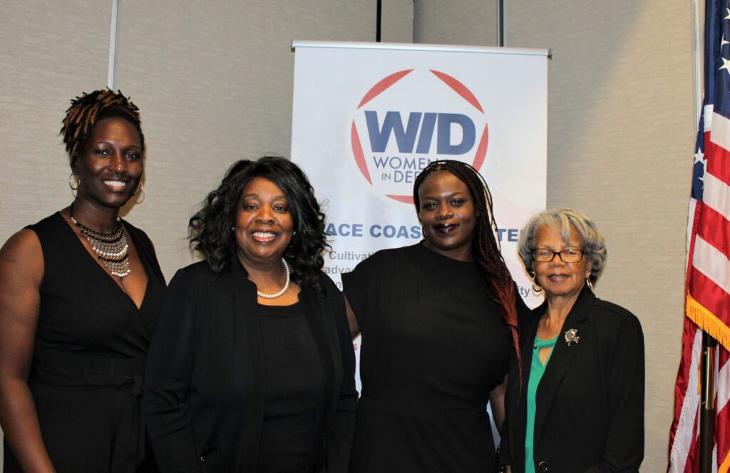 Four women standing in from of a WID poster